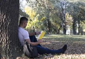 Man leaning against a tree reading a book