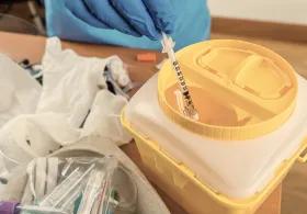 Scientist adding syringe to yellow hazardous waste bin