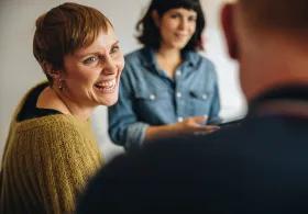 hree people in conversation, with two facing and smiling at the third whose back is to the camera