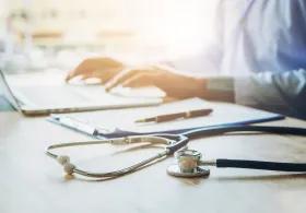 Person working at laptop with stethoscope on desk next to them