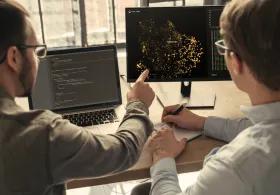 Two people discussing data at 2 computers 