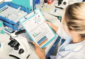 Person in lab coat looking at notes with microscope on lab bench