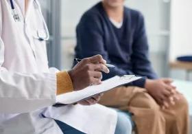 Person in white coat with stethoscope and notes talking to someone