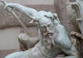 A marble statue of a muscular, bearded man with horns, gripping a staff and leaning forward in a dynamic pose. Another figure and a large shield are partially visible beside him, suggesting a mythological battle scene.