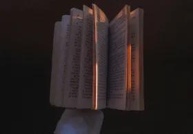 A gloved hand holding a book, with the book partially open and set against a black background