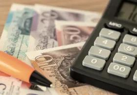 A calculator resting on British banknotes with a pen beside them on a table
