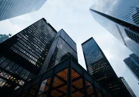 A low-angle view of several lit-up skyscrapers against a cloudy evening sky.