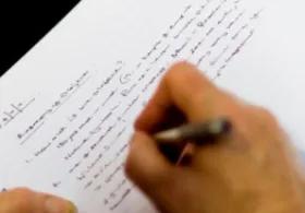 A hand holding a pen, writing in a lined notebook.