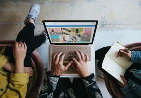 Overhead shot of three people working on a laptop and taking notes, with a Microsoft Surface Laptop displaying a photo collage on the screen.