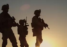 A silhouette of armed military with a yellow sunset in the background. 