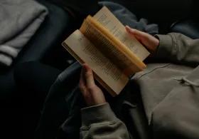 A person holds an open book, reading its pages.