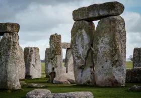 A close-up view of the massive sarsen stones and trilithons of Stonehenge under a cloudy sky, with green grass surrounding the ancient monument.