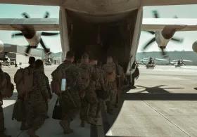 A group of military personnel, identified as US Navy SEALs, are boarding a large military transport aircraft, likely a C-130 Hercules, on an airfield with other helicopters visible in the background. 