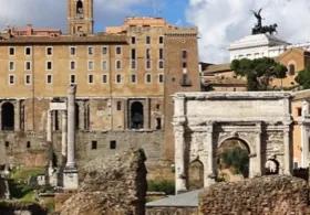 The Arch of Septimius Severus in the Roman Forum, with ruins in the foreground and other ancient structures and buildings under a cloudy sky.