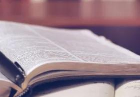 Open philosophical book with a pen resting in the center, pages slightly curved, and a softly blurred background.