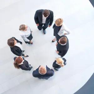Group of 8 people pictured from above, dressed in business clothing and standing in a circle. 