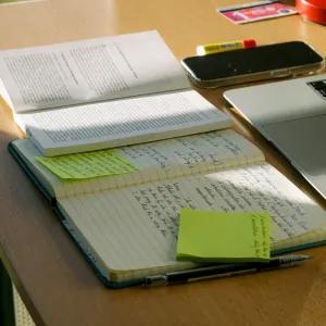 A student's desk with laptop, note book, text book and phone