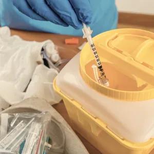 Scientist adding syringe to yellow hazardous waste bin
