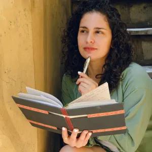 Lady holding a book with a pen in hand, thinking