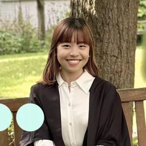 Asian woman sat on bench in graduation gown