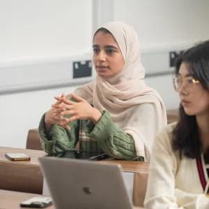 Young women sitting at desk listening to professor