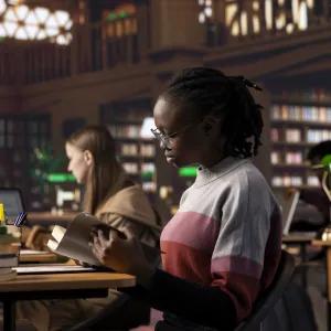 Students reading and working at desks in a quiet library setting, surrounded by shelves of books