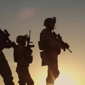A silhouette of armed military with a yellow sunset in the background. 