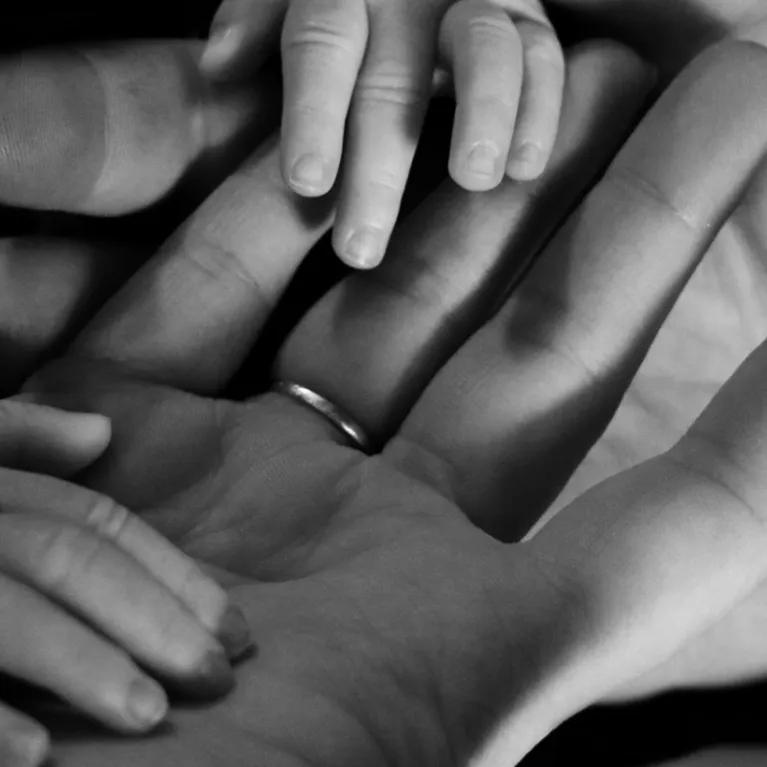 Black and white photo of 2 adult palm of hands holding baby hands. 