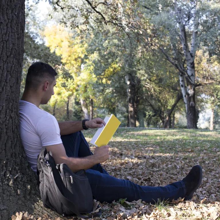 Man leaning against a tree reading a book