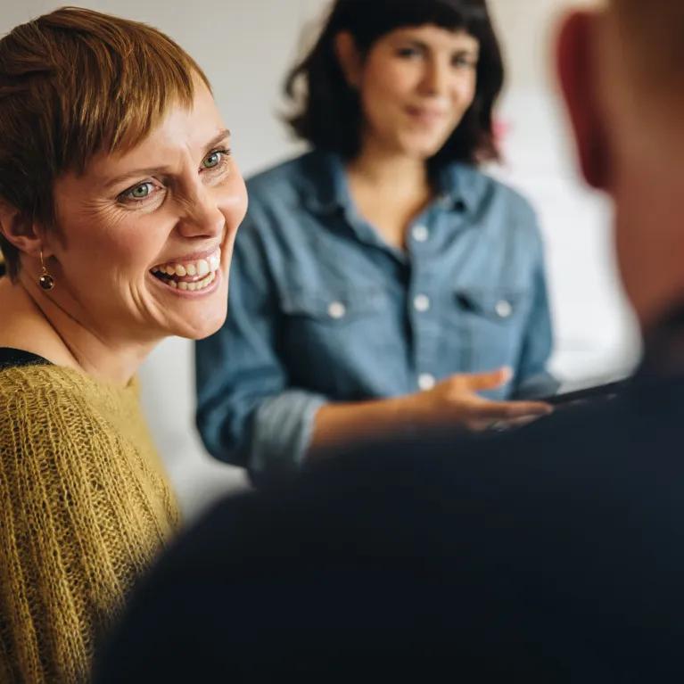 hree people in conversation, with two facing and smiling at the third whose back is to the camera