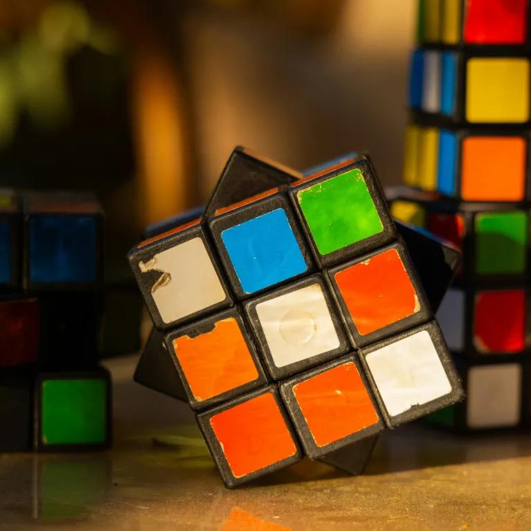 A table with 4 worn and unevenly turned Rubik’s Cubes, showing faded and peeling stickers, with mismatched colours and tilted angles