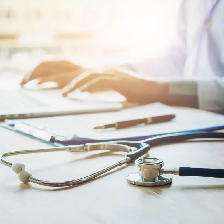 Person working at laptop with stethoscope on desk next to them
