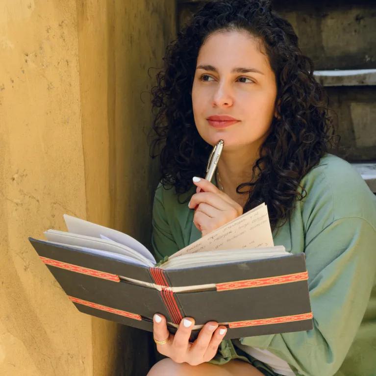 Lady holding a book with a pen in hand, thinking