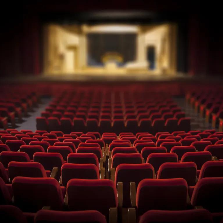 Looking down at a stage in an empty theatre of red seats