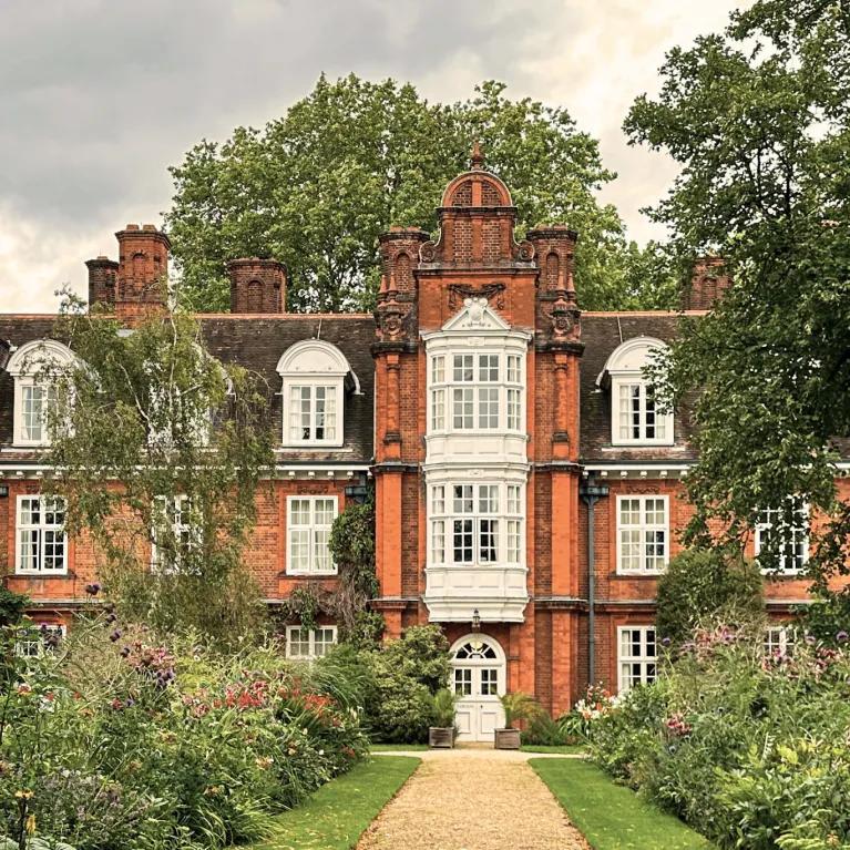 The facade of Newnham College surrounded by greenery.