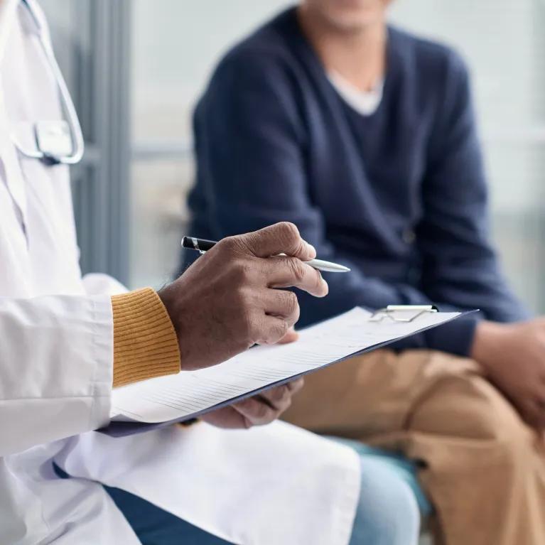 Person in white coat with stethoscope and notes talking to someone