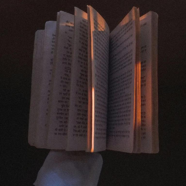 A gloved hand holding a book, with the book partially open and set against a black background