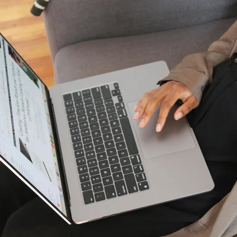 A person sitting on a sofa with an open laptop in their lap.