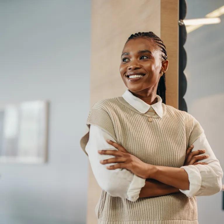 Woman standing with arms crossed smiling in office environment