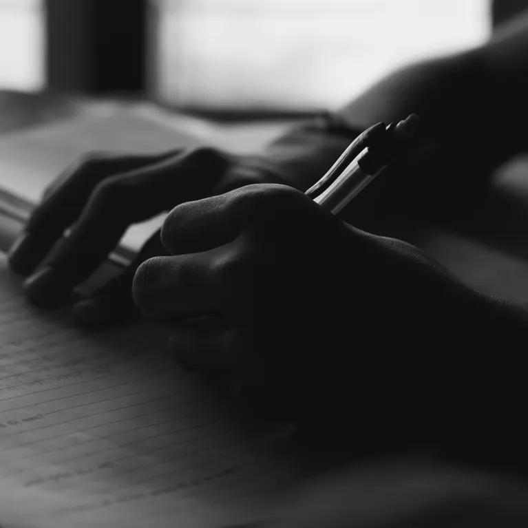 A person writing in a notepad filled with handwriting, shown in black and white