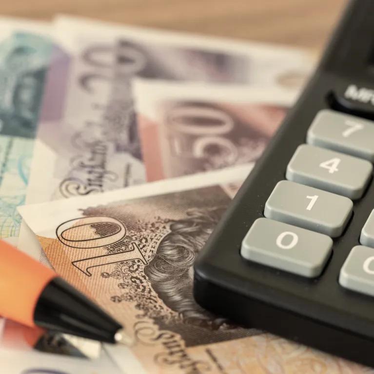 A calculator resting on British banknotes with a pen beside them on a table
