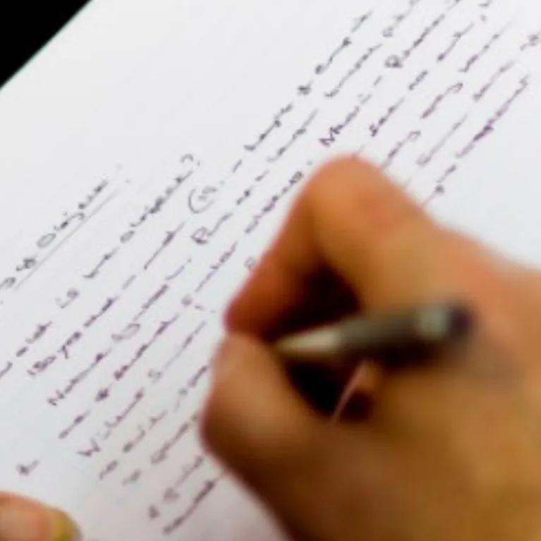 A hand holding a pen, writing in a lined notebook.