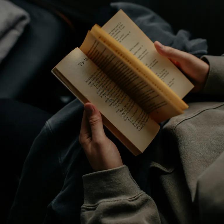 A person holds an open book, reading its pages.