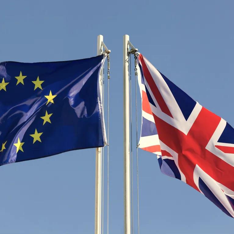 The European Union flag and the Union Jack (UK flag) flying side-by-side against a blue sky.