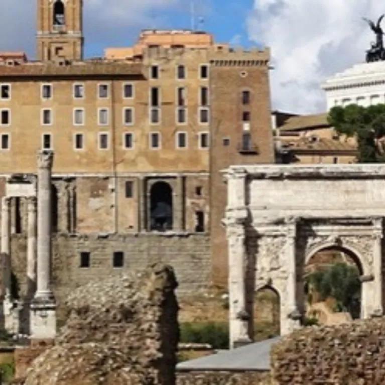 The Arch of Septimius Severus in the Roman Forum, with ruins in the foreground and other ancient structures and buildings under a cloudy sky.
