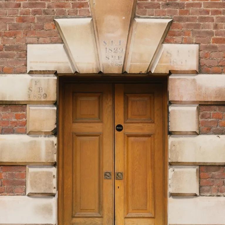 Double wooden doors set within a decorative surround of large sandstone blocks and a brick wall.