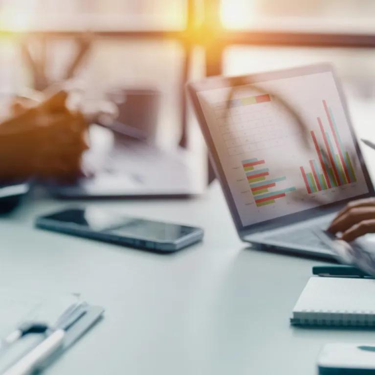 Cropped shot of people sitting on either side of a table, only their arms and hands visible, and an open laptop.