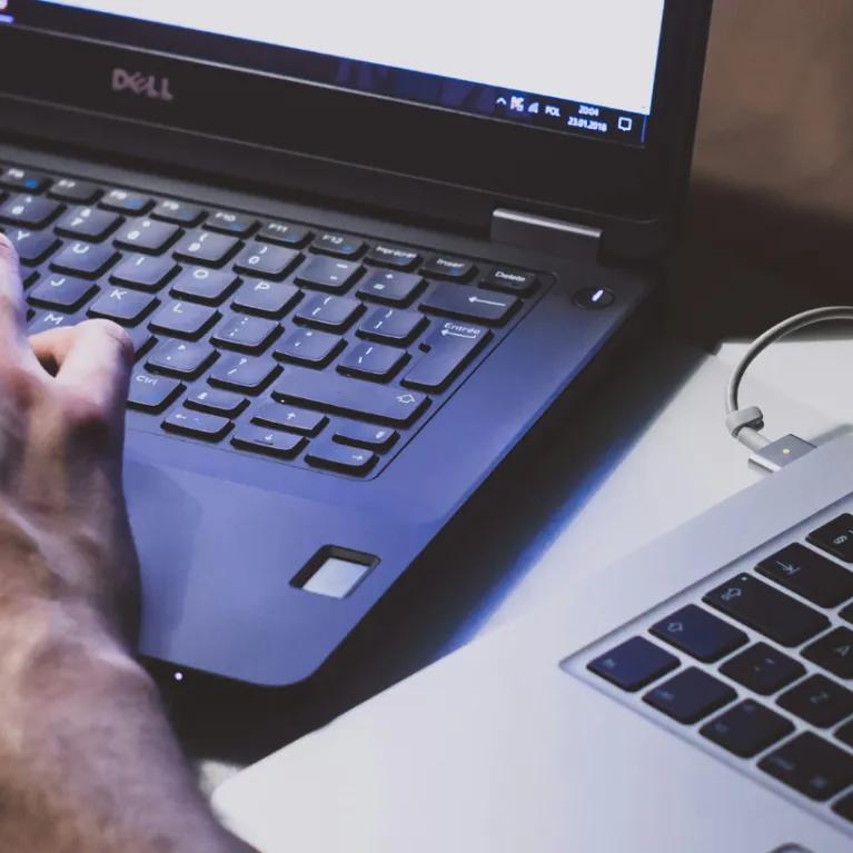 Close-up of a person's hands as they're working at a black laptop, another open silver laptop next to it.