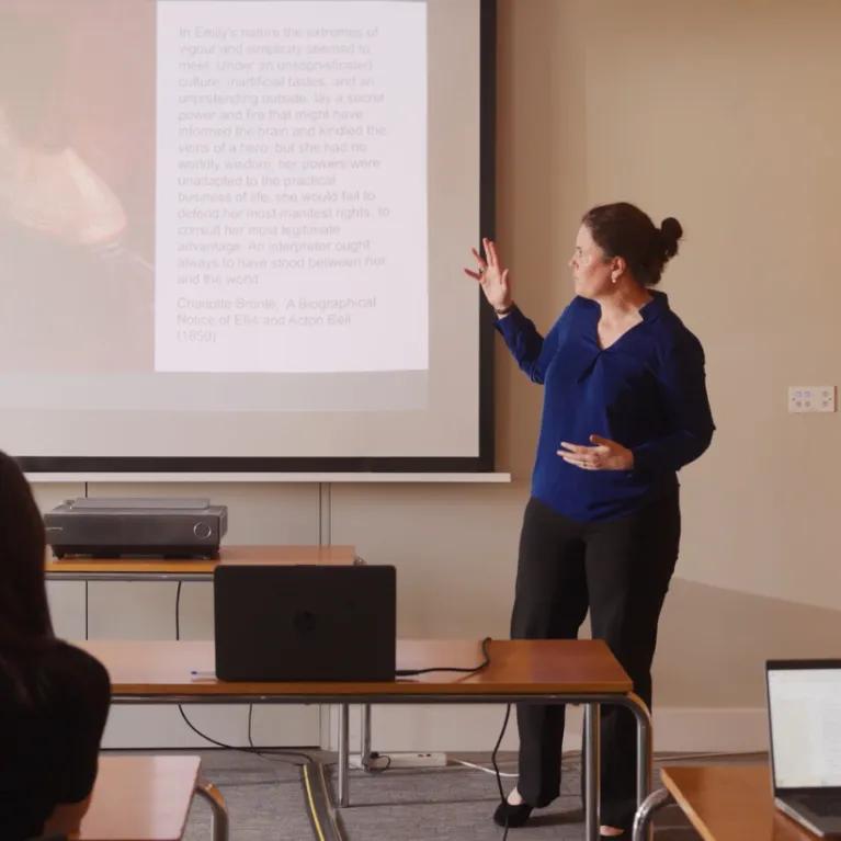 A woman stands and presents at the front of a classroom.