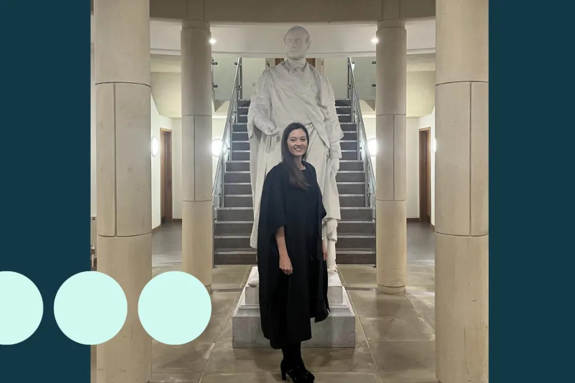 Woman in graduation gown stood in front of a statue 